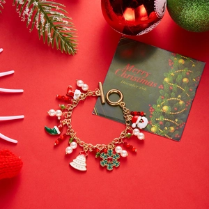 Close-up of golden Christmas charm bracelet with Santa and snowflake charms on festive red background