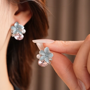 Détail de boucles d'oreilles fleur bleue avec pierre rose et perles portées par modèle
