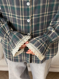 Detail of plaid shirt sleeve featuring beige floral lace cuffs and white buttons