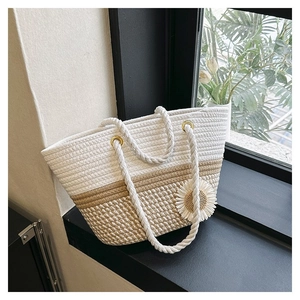 Detail of woven straw bag with white flower charm and braided handles on a window sill