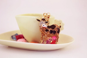 Detail of cute cow keychain with brown crystals and black enamel in a teacup setting