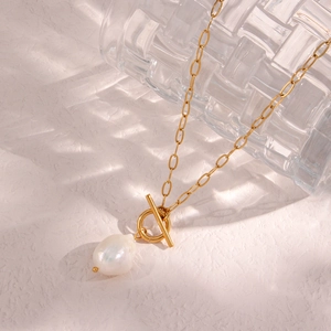 Minimalist gold necklace with baroque pearl pendant and OT toggle clasp on textured background