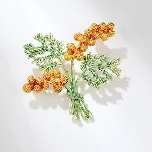 Close-up of golden pine cone brooch with green crystals and elegant branch detail
