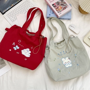 Detail view of red and light green drawstring tote bags with floral rabbit embroidery