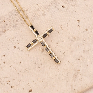 Detail of 18K gold cross necklace with black and white zircon on beige stone surface