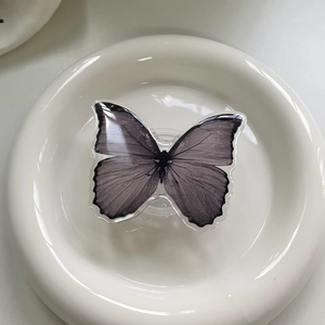 Close-up of a grey gradient butterfly expandable phone stand on a white ceramic tray