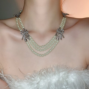 Detailed view of elegant triple-layer pearl necklace with silver bow tie crystal accents