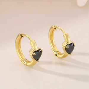 Detail shot of golden heart earrings with black gemstones on a minimalist warm background