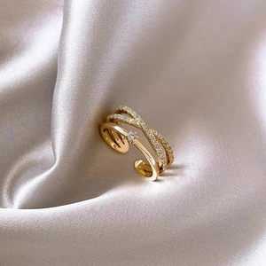 Detailed close-up of double-layer crisscross gold ring with zircon stones on silk fabric