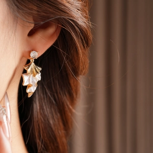 Detail of model wearing gold and white layered leaf earrings with a sparkling zircon stud