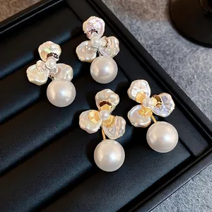 Elegant gold and silver flower petal earrings with large round pearls on black tray
