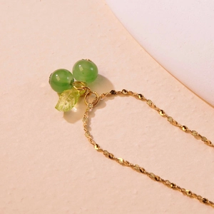 Close-up of golden cherry necklace with green bead pendants and leaf detail