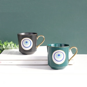 Detailed view of evil eye ceramic mugs in matte black and green with gold handle accents