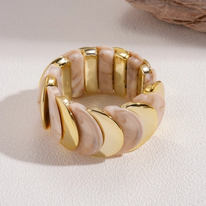 Vista macro di archi in metallo dorato e resina marmorizzata beige su un bracciale elastico