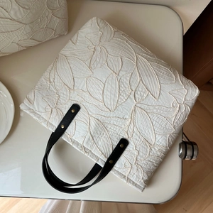 White canvas tote bag with embroidered leaf patterns and black faux leather handles