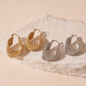 Textured gold and silver chunky teardrop hoop earrings on marble display stand
