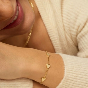 Close-up of elegant gold heart charms on a delicate chain bracelet worn with a sweater