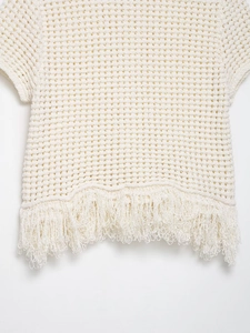 Détail de la maille crochetée blanche et des finitions à franges sur ce haut en tricot