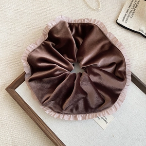 Detail of a large dark brown velvet scrunchie with elegant lace trim on a wooden tray