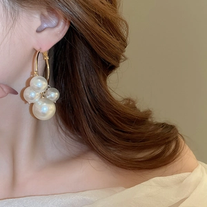 Detailed close-up of gold metal hoop earrings featuring clustered white pearls on a model