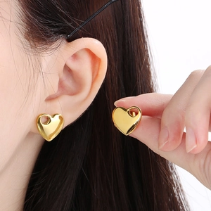 Detail of hollow heart-shaped gold stud earrings worn by model showing glossy metal finish