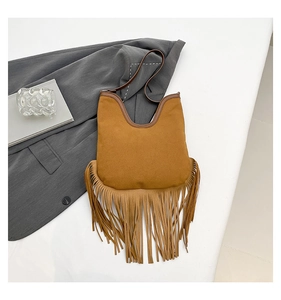 Detail view of brown suede shoulder bag with long fringes in bohemian style on a white fabric