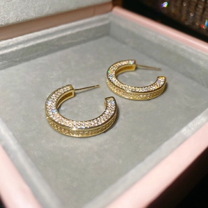 Detailed macro view of gold-plated C-shaped earrings with sparkling pave-set cubic zirconia