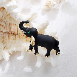 Detail of an elephant brooch in matte black with gold accents and a green crystal eye