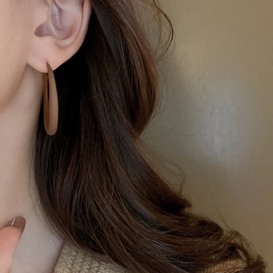 Close-up of elegant matte brown hollow hoop earrings worn by a model in warm light