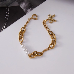 Golden titanium steel bracelet with three pearls and a bow charm on white background