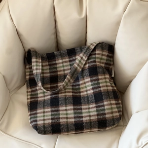 Détail d'un grand sac cabas en laine à carreaux rétro sur un fauteuil crème doux