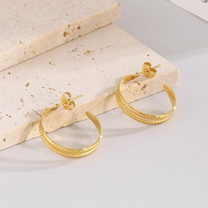 Detailed view of C-shaped golden earrings with braided wheat texture on beige stone stairs