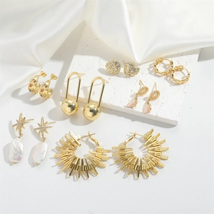 Detailed close-up of various gold-plated earrings set on a white stone and silk texture