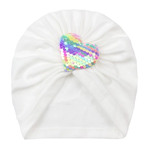 Détail d'un turban pour bébé avec un cœur en paillettes arc-en-ciel sur tissu blanc
