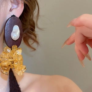 Detail of wooden drop earrings with white pearl inlay and yellow resin stones on a model