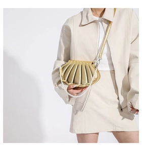 Detail einer goldenen muschelförmigen Umhängetasche mit Perlenhenkel und Metallic-Finish