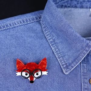 Fashionable red fox acrylic brooch with glasses pinned on a blue denim shirt collar
