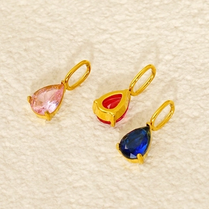 Close-up of three teardrop birthstone pendants in pink, red, and blue with gold settings