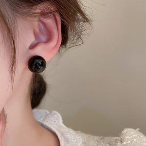 Close-up of minimalist large black spherical stud earrings with a polished mirror finish