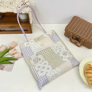 Close-up of patchwork tote bag with floral patterns and lavender handles on a white desk
