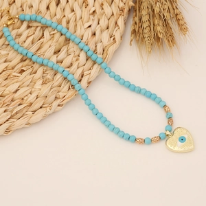 Bohemian turquoise beaded necklace with golden heart evil eye pendant on a rustic background