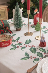Detail of Christmas tablecloth with holly leaf patterns and festive table decorations