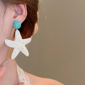 Close-up of woven raffia starfish earrings in white and teal worn by a model