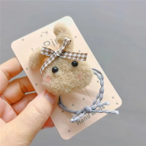 Detail of plush beige rabbit hair tie with brown plaid bow on pink star card