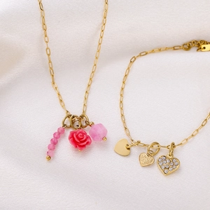 Detail view of gold paperclip chain jewelry set with pink rose pendant and heart charms