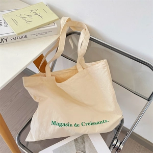 Detail shot of a canvas tote bag with green French text on a transparent chair