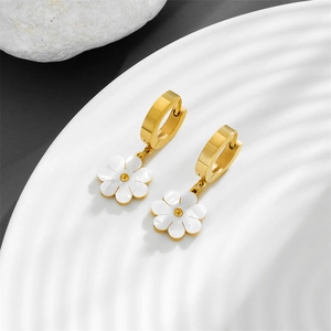 Detail of gold daisy earrings with white enamel petals on a textured stone surface