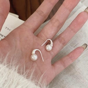 Minimalist 925 sterling silver pearl hook earrings held by hand over a cozy sweater background