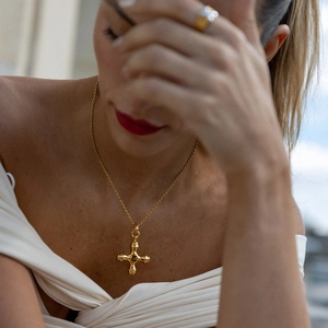 Detail of 18k gold cross necklace with tiger eye stone on a model with twisted chain