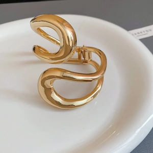 Macro shot of gold irregular wave bangle featuring high polish finish and hinge detail